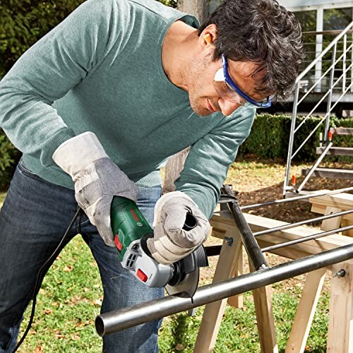 Hombre usando amoladora angular en tubo metálico.